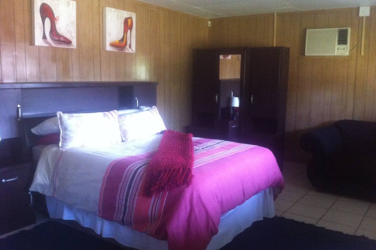 Une chambre d’hôtel comprenant un lit, une table de chevet, une chaise et une porte donnant sur une autre pièce.