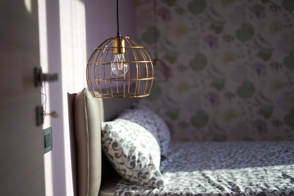 Une pièce avec un lit, un mur décoré d’un motif et un luminaire suspendu.