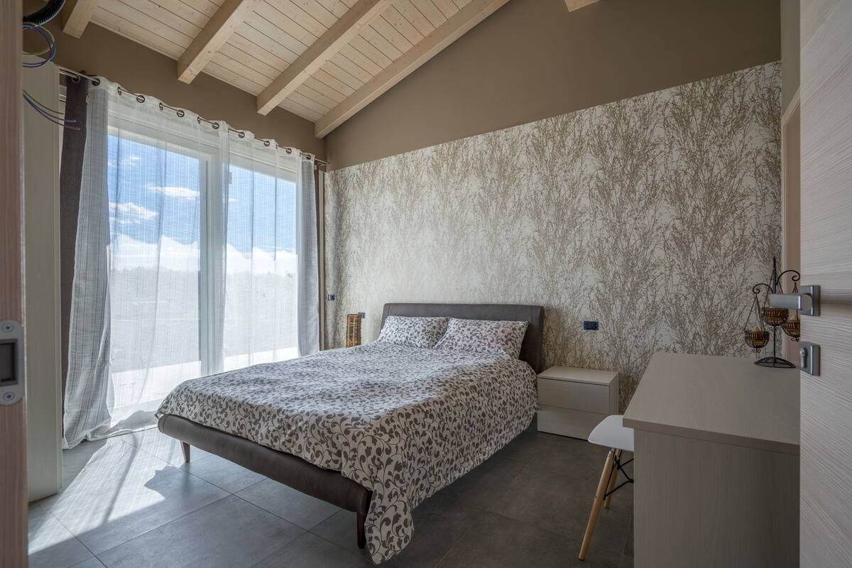 Une chambre à coucher avec un lit, des tables de chevet, un bureau et une fenêtre avec des rideaux.