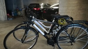 Polkupyörä on pysäköity autotalliin, jonka lattia on betoninen, ja taustalla näkyy auto.