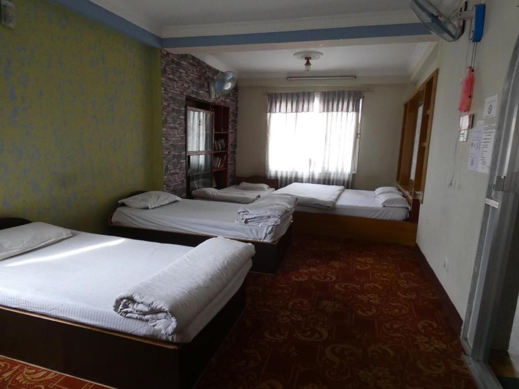 Habitación de hotel con tres camas individuales, un escritorio pequeño, una estantería y una ventana con cortinas.