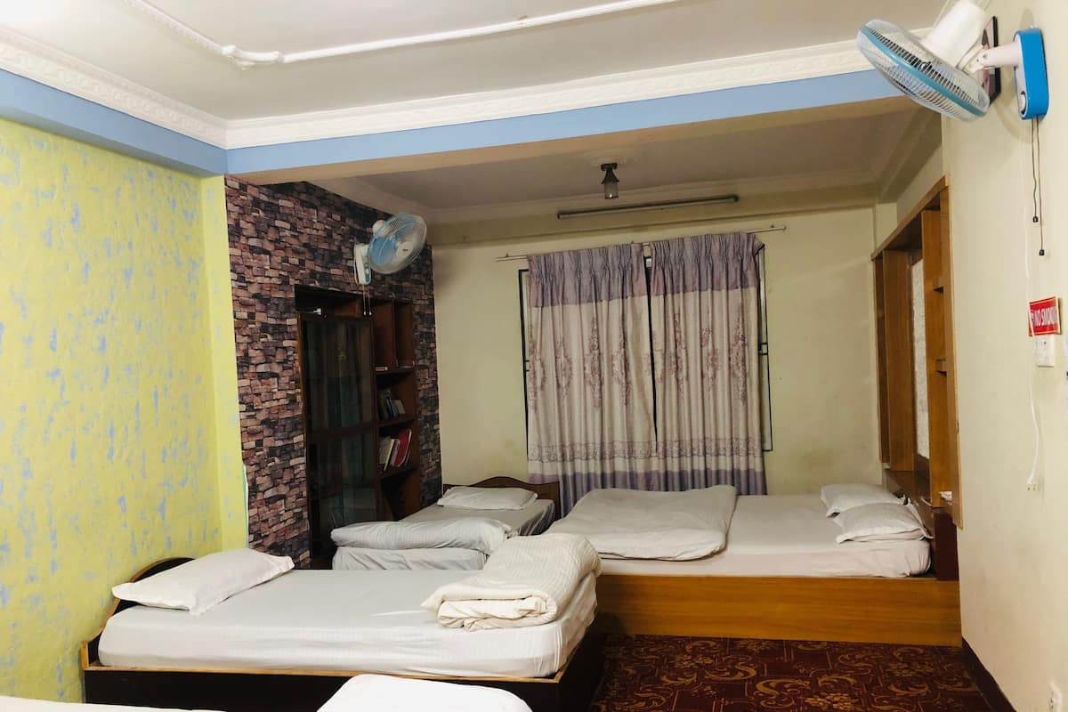 Una habitación con tres camas, una pared de ladrillo, un ventilador y una alfombra estampada.
