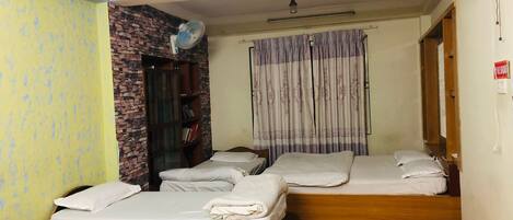 A room with three beds, a brick wall, a fan, and a patterned carpet.