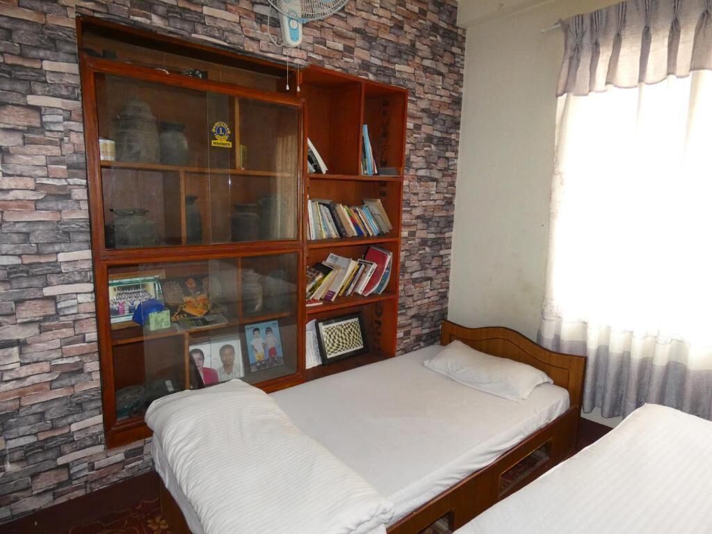 A room with two beds, a bookshelf, and a window with curtains.