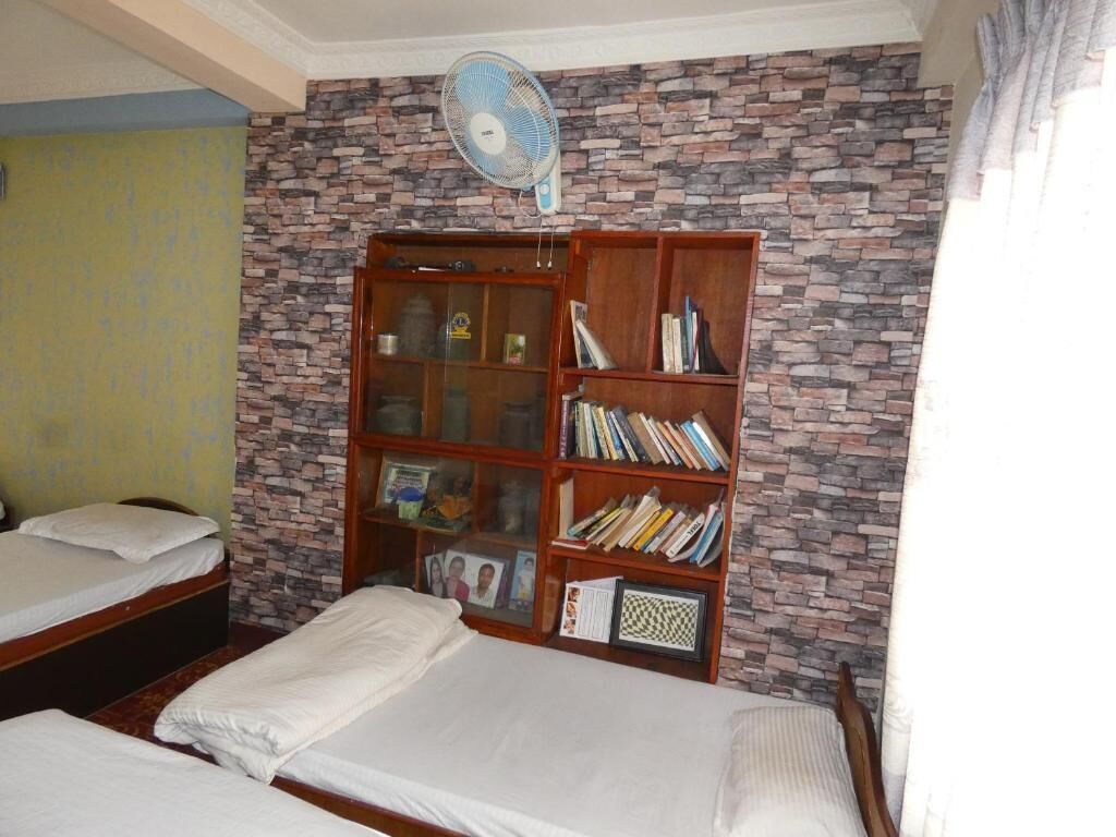 Una habitación con dos camas, una estantería y un ventilador.