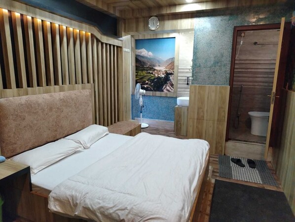 A modern bedroom with a large bed, a wooden headboard, a small bedside table, and a bathroom visible through an open door. - Sara's Backpackers Hotel (Tohka)