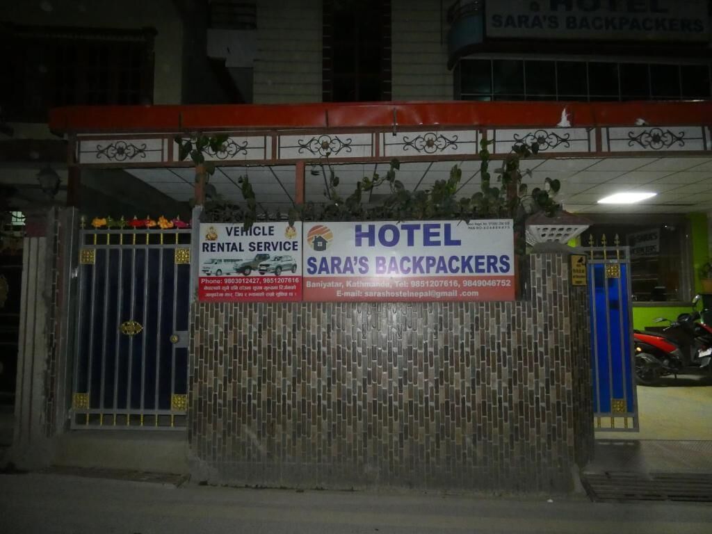 A hotel entrance with a sign for 'SARA'S BACKPACKERS' and a vehicle rental service.