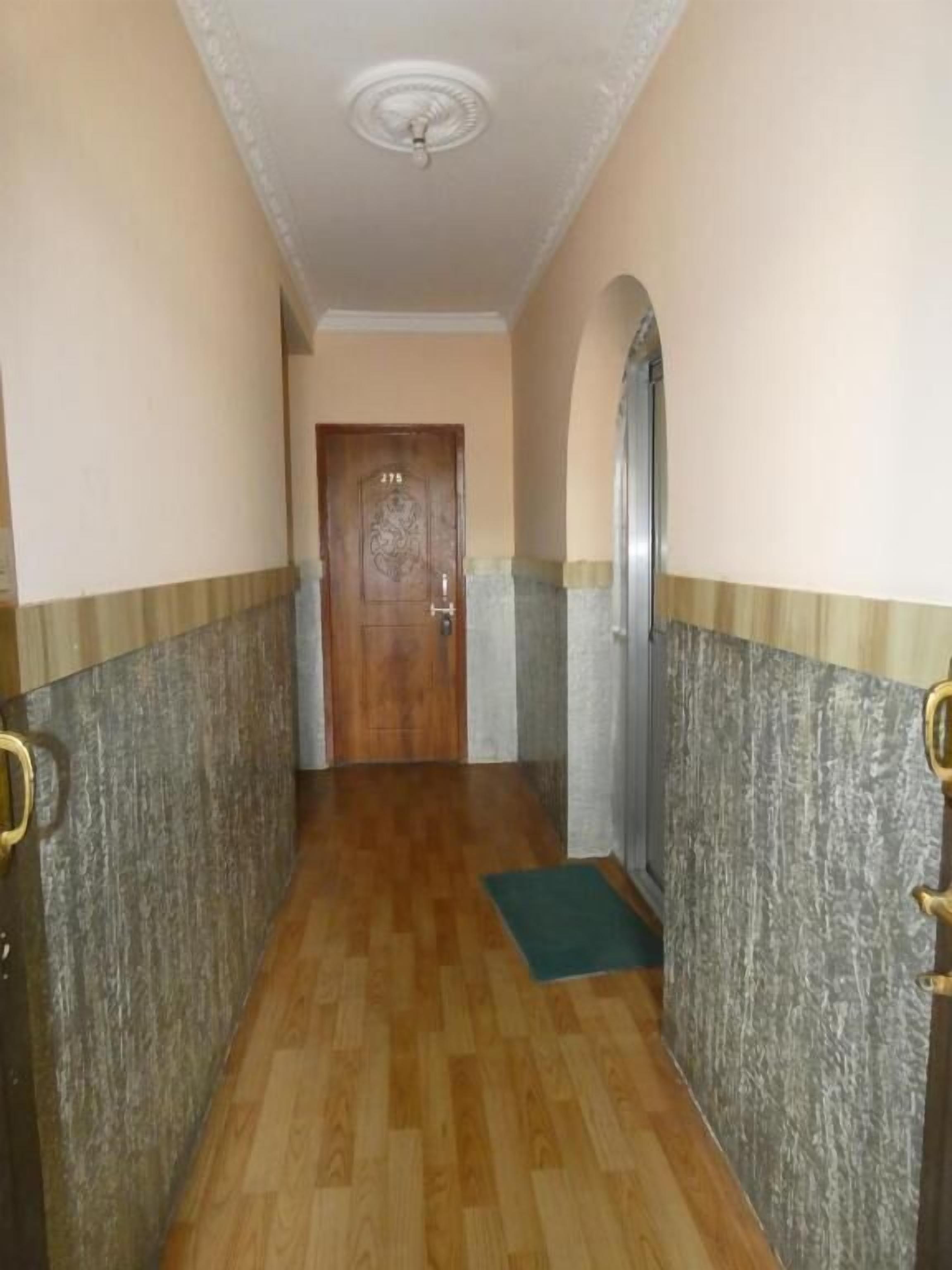 A hallway with a wooden floor, a door at the end, and a green mat on the floor.