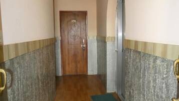 A hallway with a wooden floor, a door at the end, and a green mat on the floor.