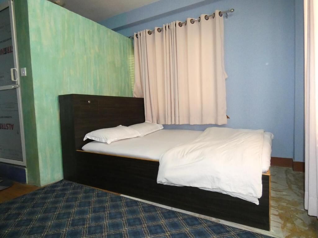 Una cama individual con cabecera de madera en una habitación con paredes azul claro y alfombra estampada.
