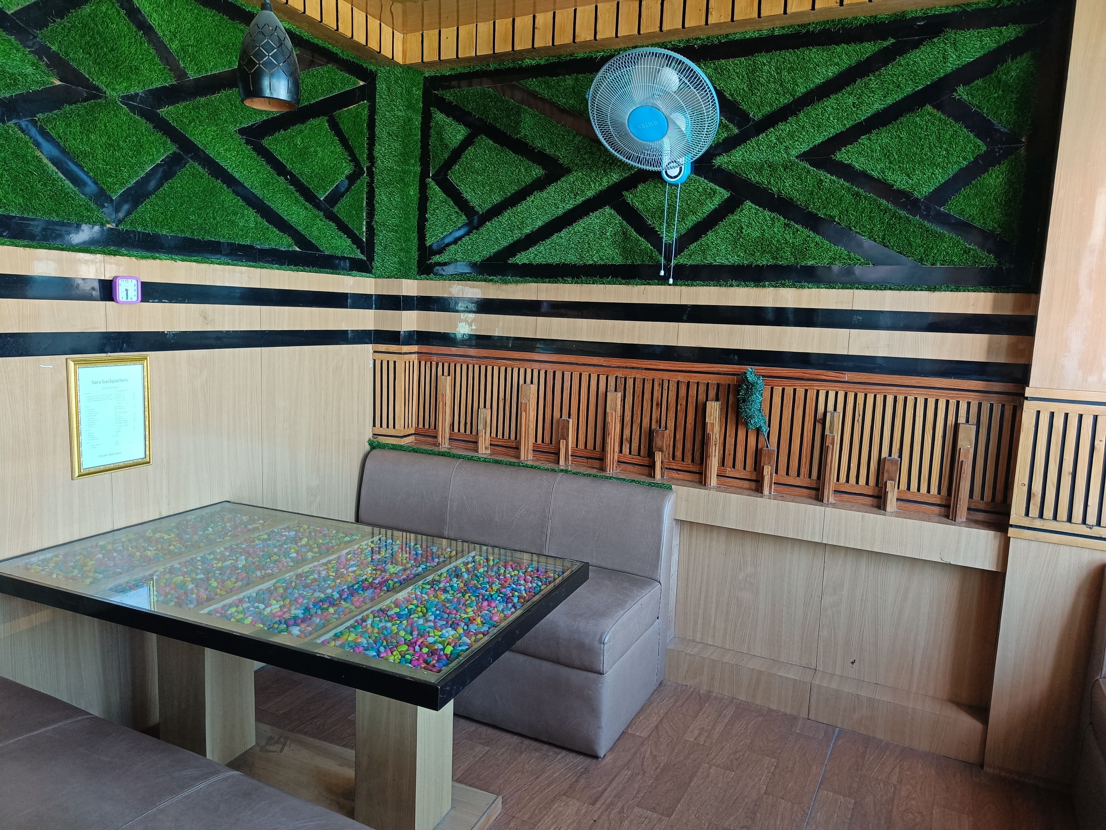 A room with a glass-top table filled with colorful pebbles, a bench, a wall clock, and a fan.