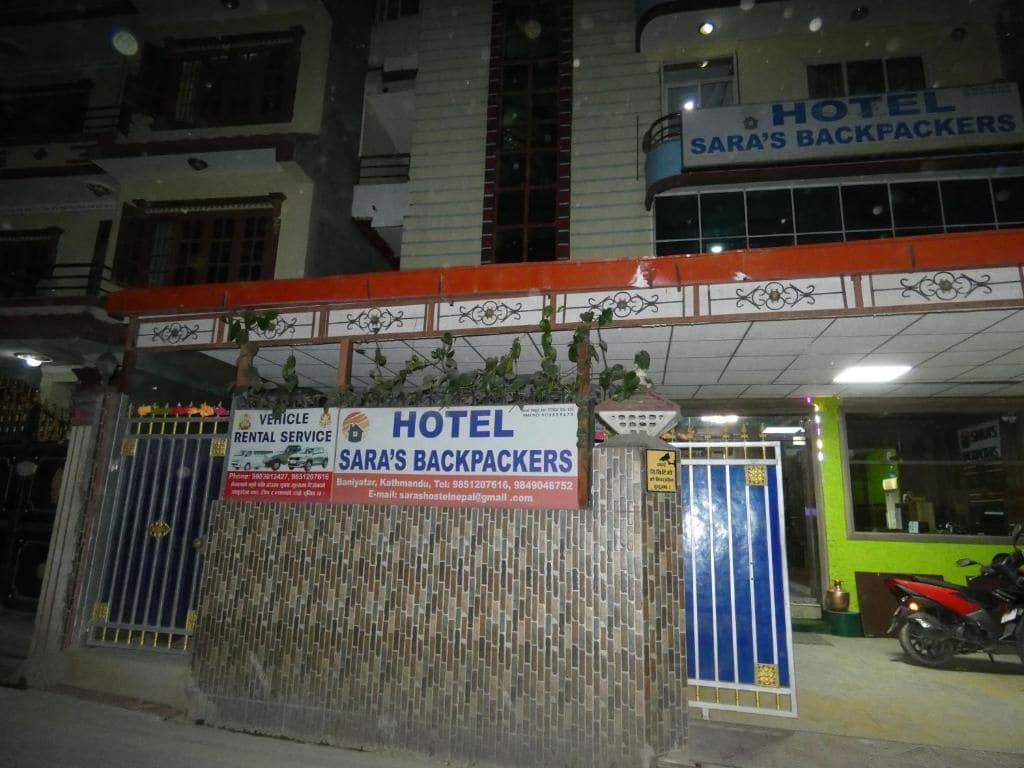 A hotel entrance with a sign for 'SARA'S BACKPACKERS' and a vehicle rental service.