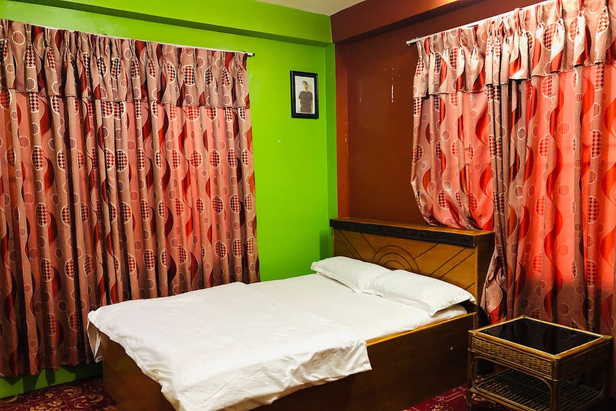 Una cama individual con sábana blanca en una habitación con paredes verdes y cortinas estampadas.