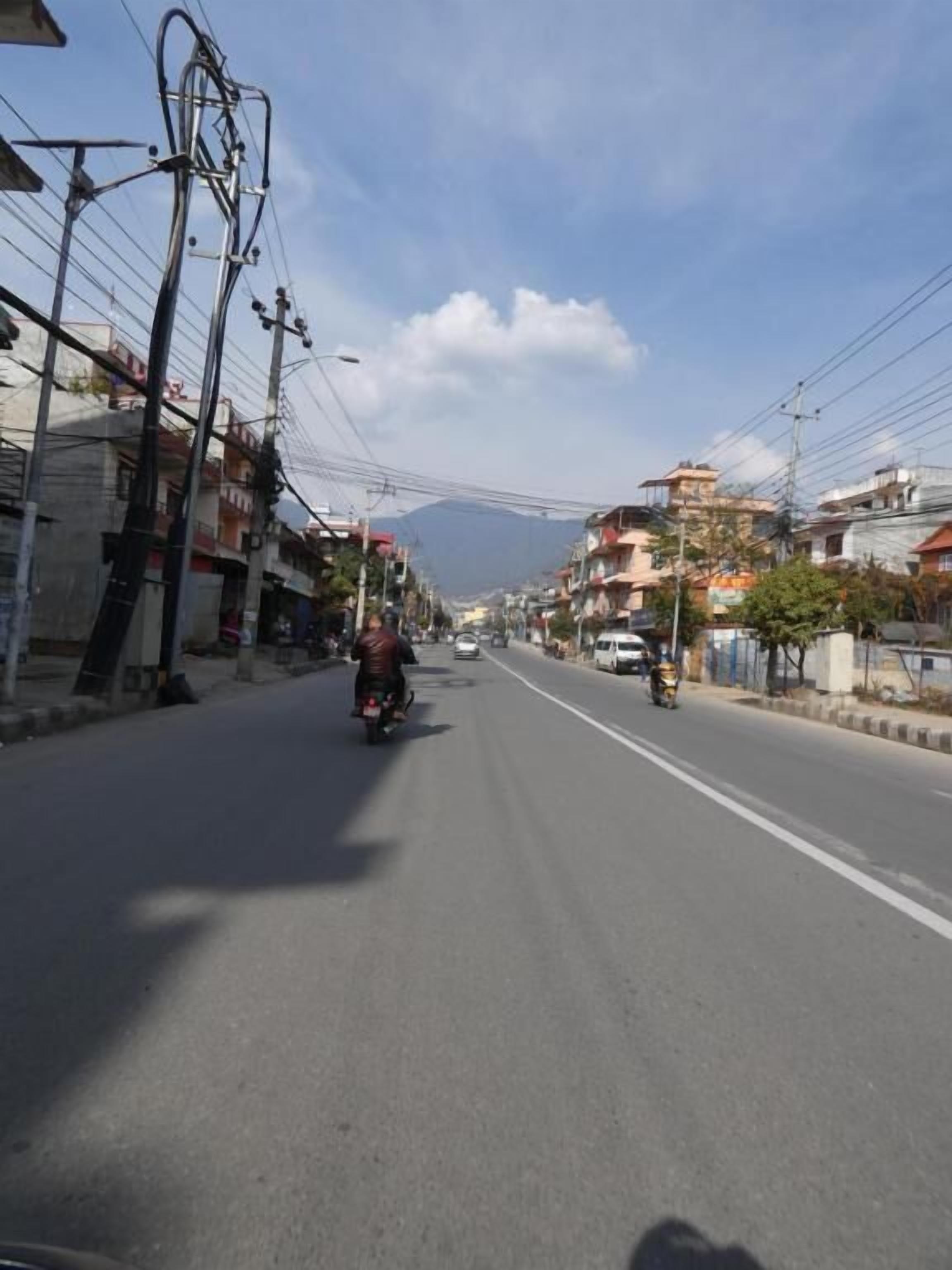 Uma rua com edifícios em ambos os lados, céu claro e uma moto à distância.