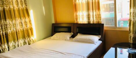 A hotel room with a bed, a bedside table, and curtains.