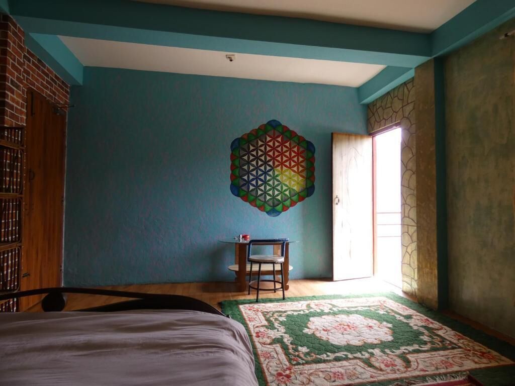 A bedroom with a bed, a chair, a patterned rug, and a geometric wall decoration.