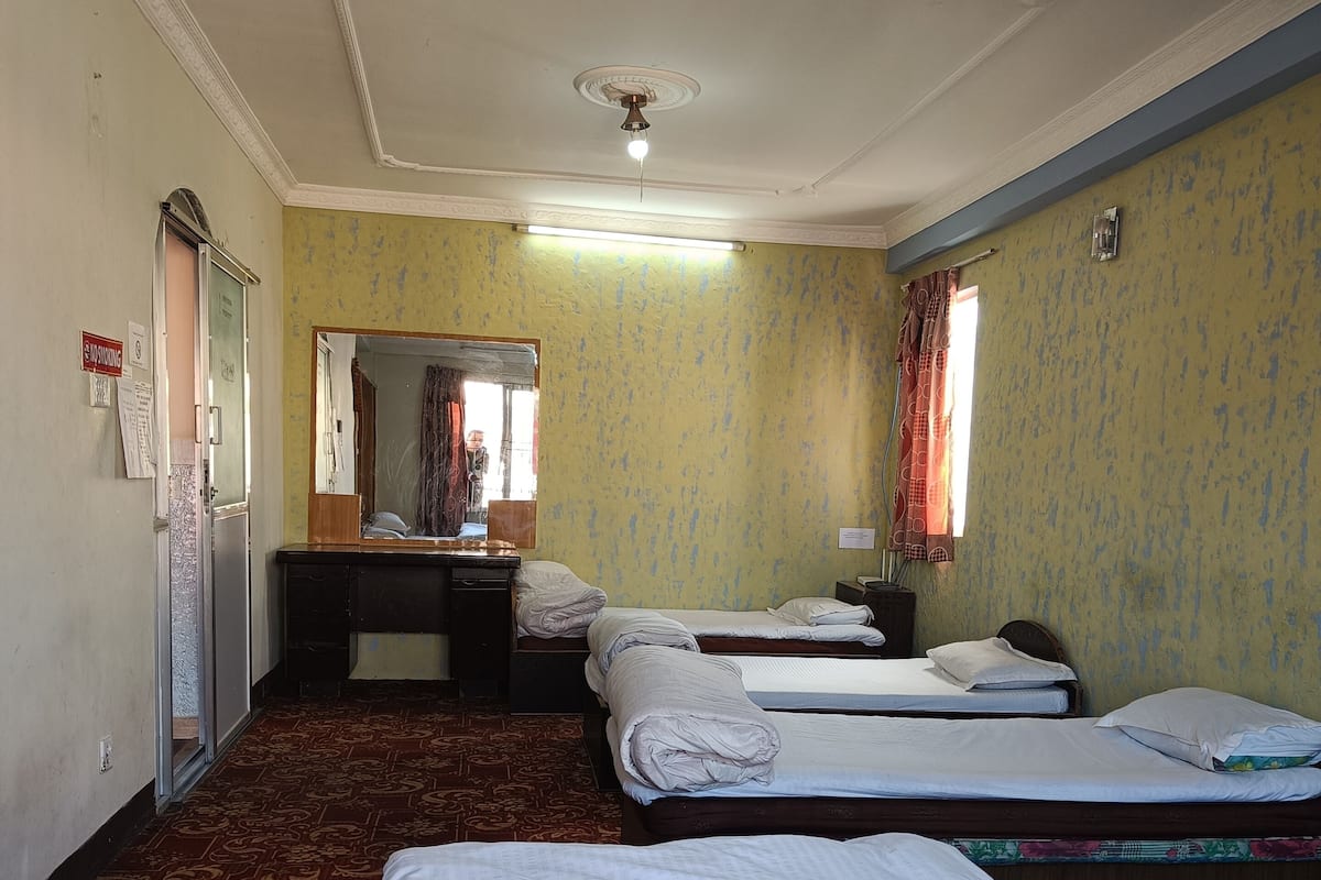 Habitación de hotel con dos camas, un escritorio con espejo, ventilador de techo y ventana con cortinas.