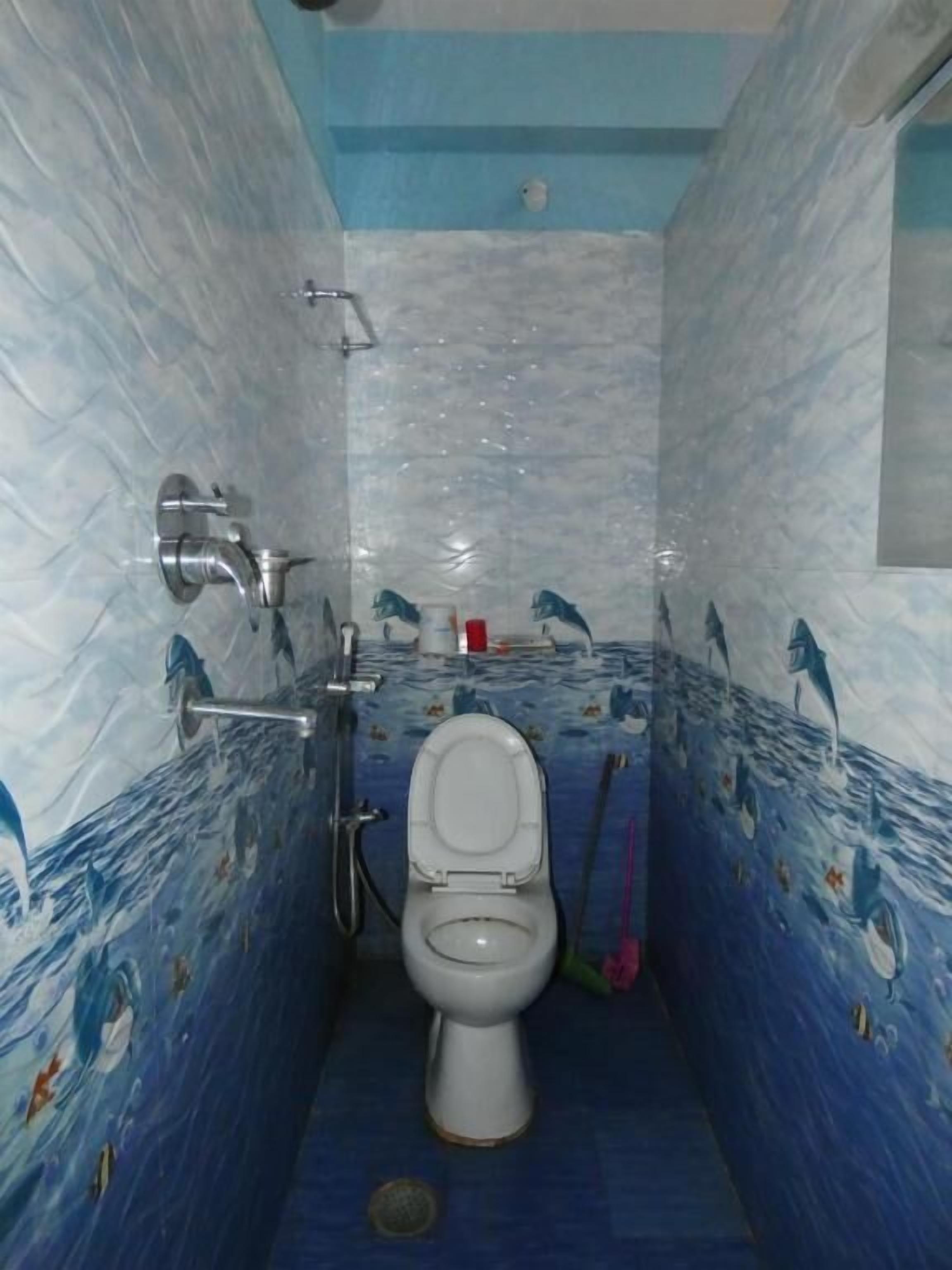 A bathroom with a white toilet, blue tiled walls, and a shower area.