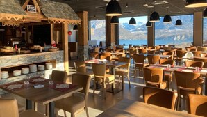 Un restaurante con mostrador de piedra y sillas de madera, amplias ventanas con vistas a la montaña e iluminación colgante.