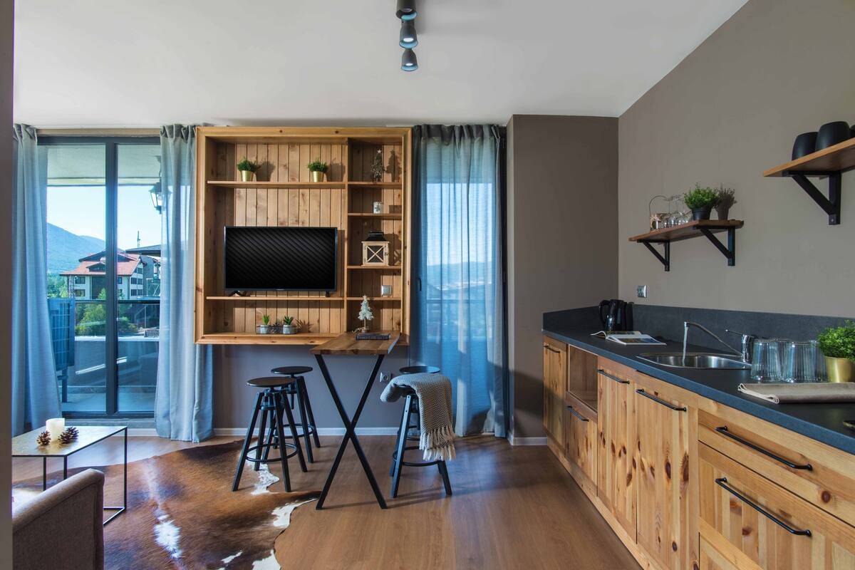 A modern kitchen with wooden cabinets, a bar area, and a large window with curtains.