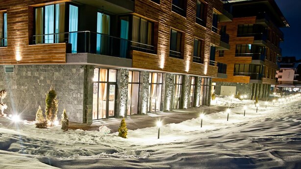 Un edificio moderno de varios pisos con grandes ventanales y fachada de piedra, rodeado de nieve.