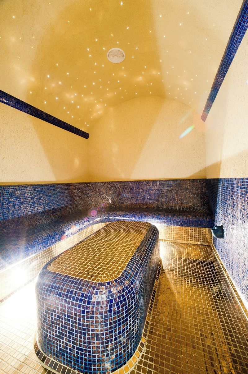 A room with a mosaic-tiled bathtub, a ceiling with a starry design, and a wall with a blue mosaic pattern.