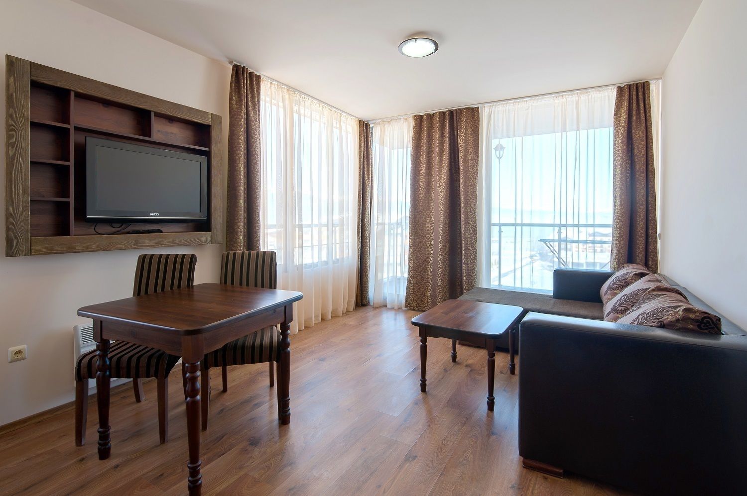 Una sala de estar con una mesa de comedor de madera, dos sillas, un sofá y un televisor montado en la pared.
