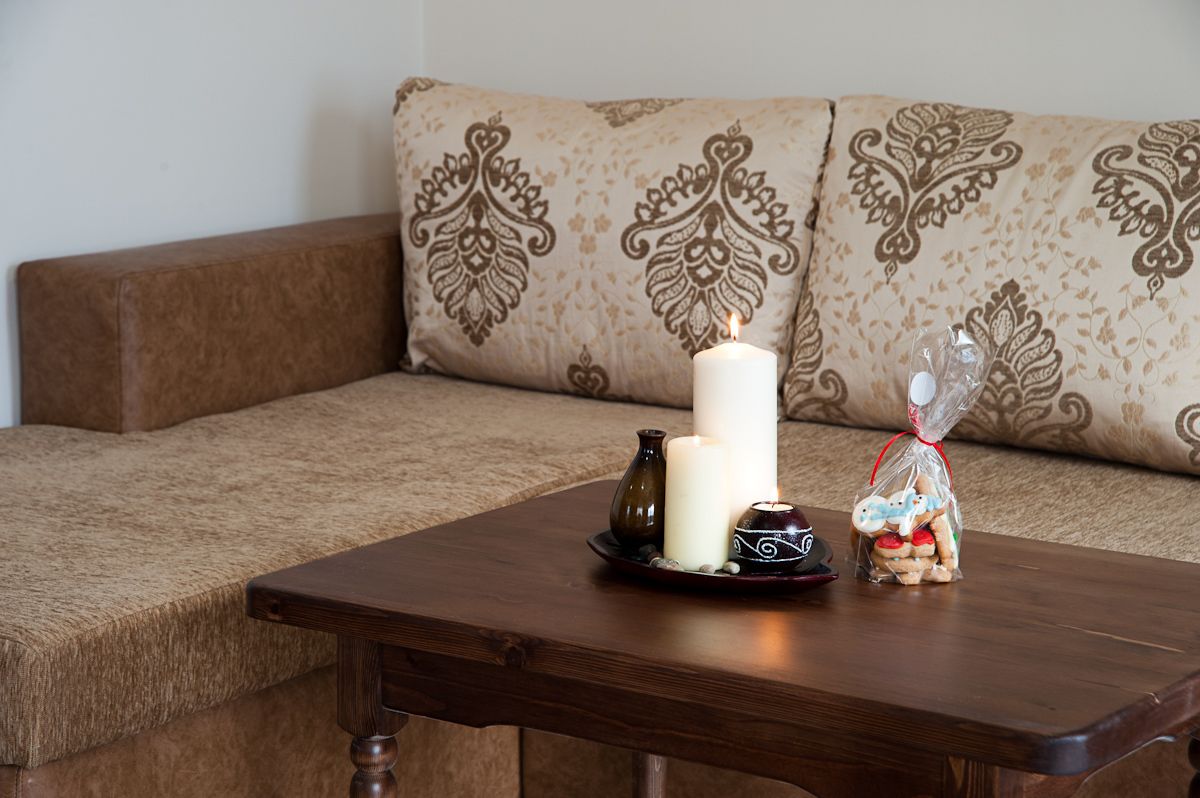 Una mesa de madera con una vela, un florero y un adorno sobre un sofá estampado.
