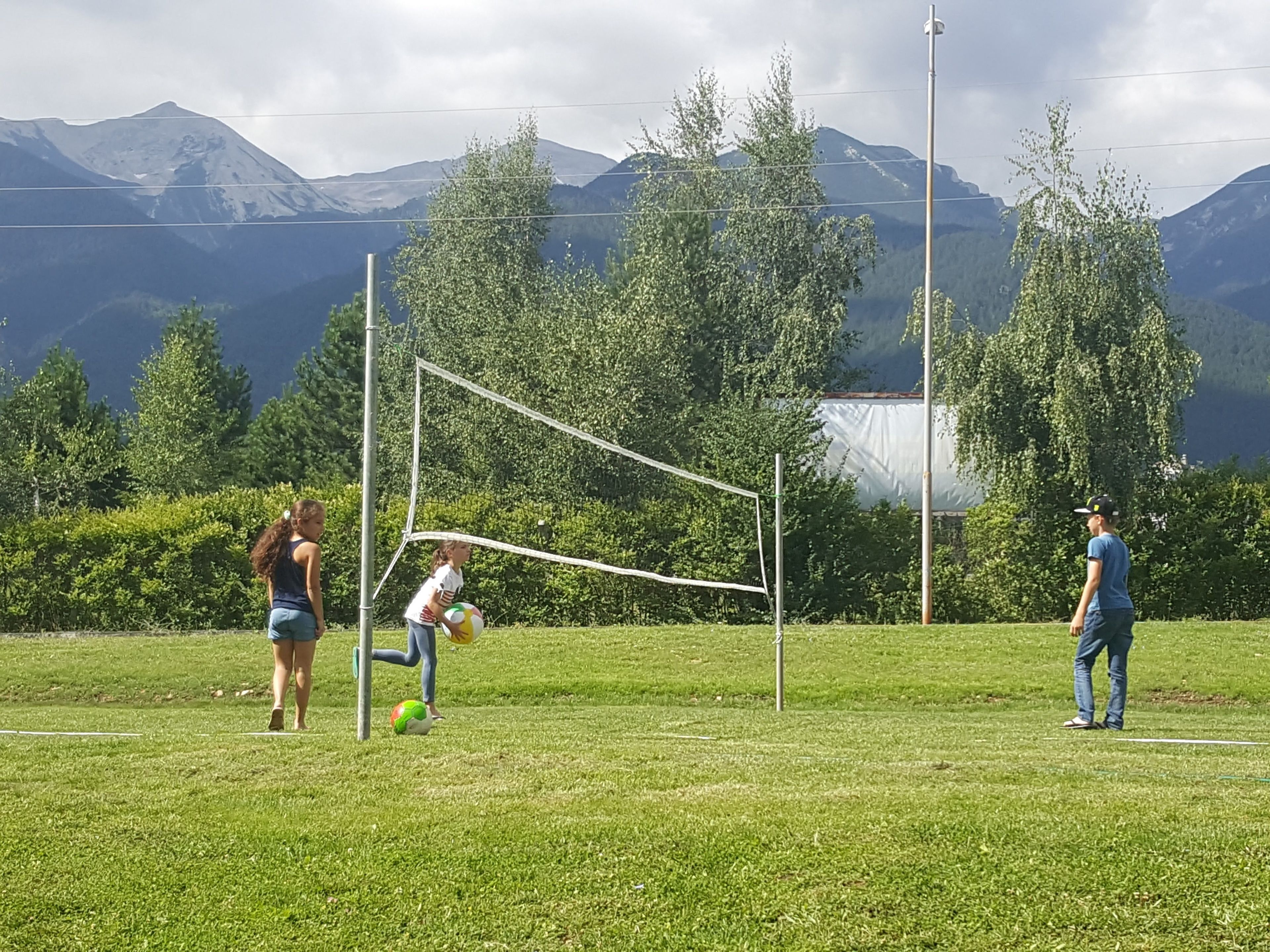 A volleyball game in a grassy field with mountains in the background.