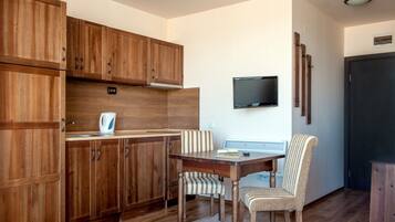 Una cocina compacta con armarios de madera, un microondas integrado, una mesa de comedor con dos sillas a rayas y un televisor de pantalla plana montado en la pared.