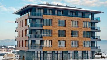 A multi-story modern building with balconies, large windows, and a view of the mountains.
