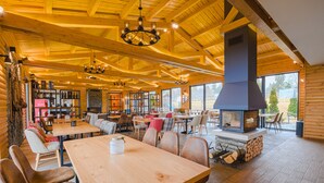 Interior acogedor de una cabaña de troncos con mobiliario de madera, chimenea y ventanas amplias.