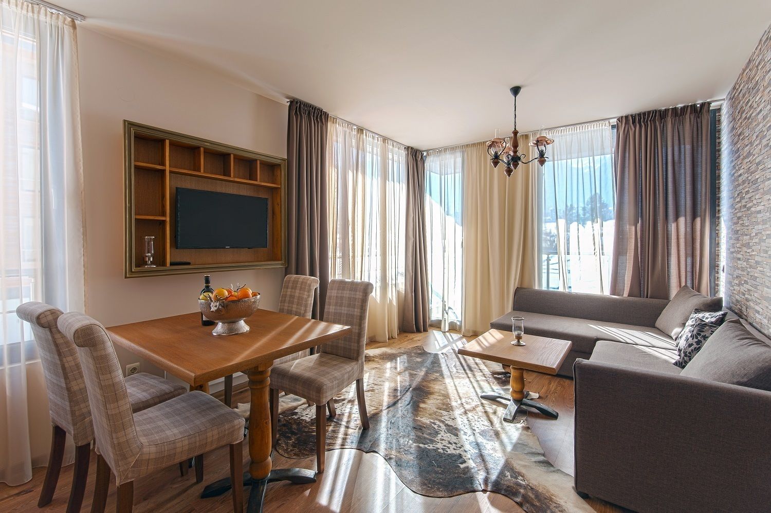 Uma sala de estar moderna com uma mesa de jantar de madeira, dois sofás e uma TV presa na parede.