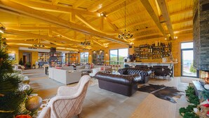 Amplia sala de estar con techo alto, vigas de madera, chimenea y zona de bar con estantes llenos de botellas.
