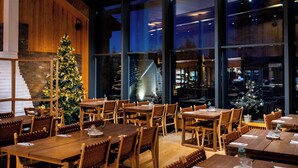 Un restaurant avec des tables et des chaises en bois, un sapin de Noël et de grandes fenêtres donnant sur la ville.