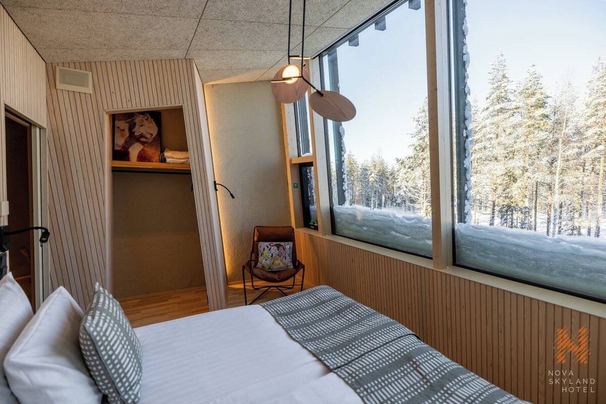 Een gezellige kamer met een bed, een stoel en een groot raam met uitzicht op een besneeuwd bos.