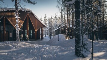 Una cabaña de madera con techo inclinado, rodeada de árboles cubiertos de nieve y un cielo despejado.