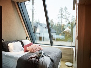 A bedroom with a large window, a bed with pillows and a blanket, and a bedside lamp. - Nova Skyland Hotel (Rovaniemi)