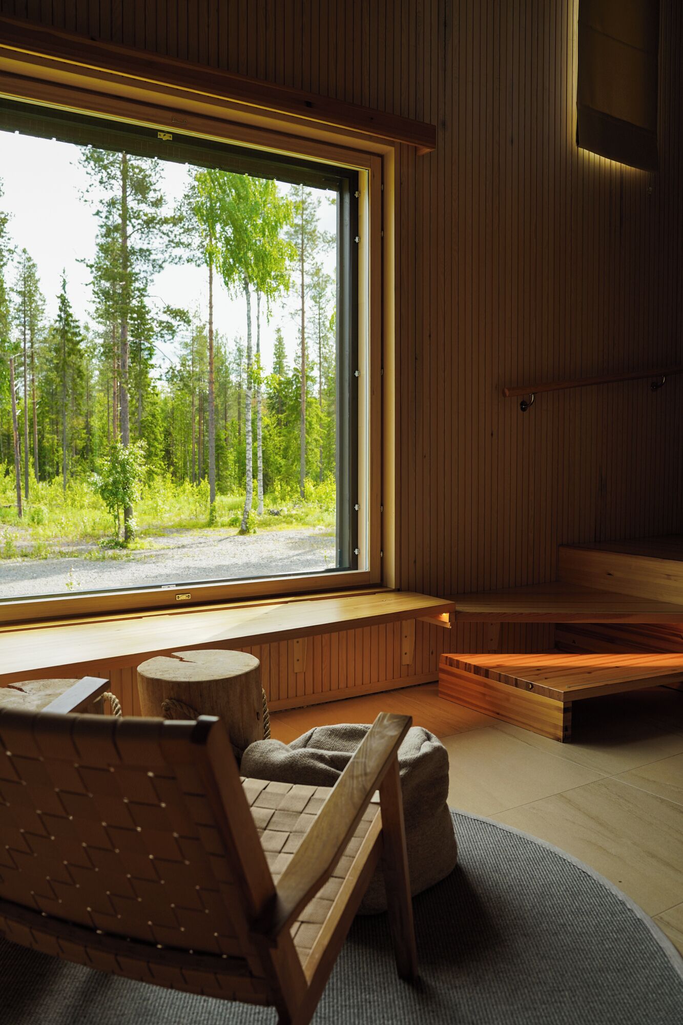 A modern cabin with a large window offering a view of a forest. Inside, there is a wooden bench and a small table.
