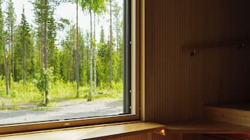 A modern cabin with a large window offering a view of a forest. Inside, there is a wooden bench and a small table.