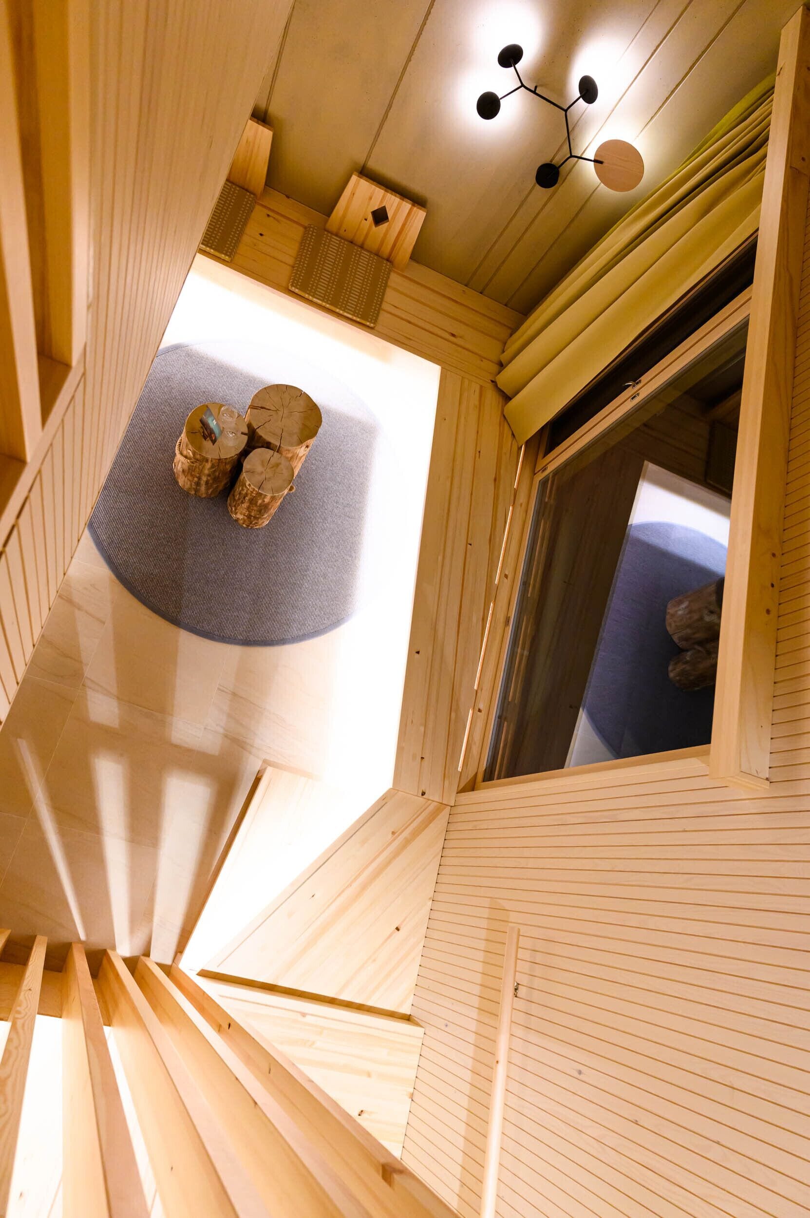 Una escalera de caracol con barandillas de madera y vistas a una habitación con ventana y lámpara en el techo.