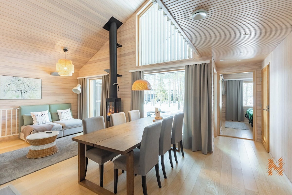 Een ruime kamer met een houten plafond, een eettafel met stoelen, een bank en een open haard.