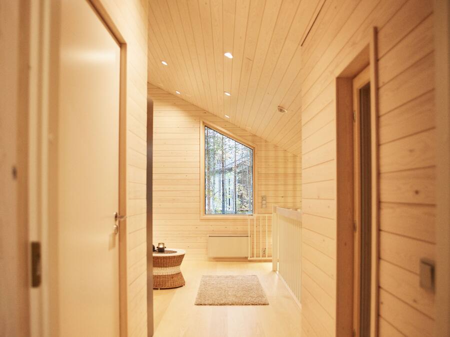 A wooden interior hallway with a large window, a radiator, and a small wicker stool.