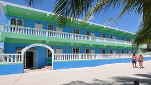 A hotel with a blue and green facade, a white balcony, and a rainbow arch. - Rainbow Hotel (Caye Caulker)