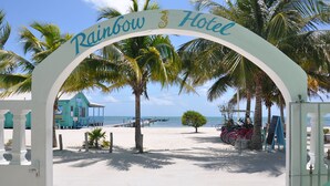 A beach entrance with a sign reading "Rainbow Hotel," palm trees, a beach, and bicycles. - Rainbow Hotel (Caye Caulker)
