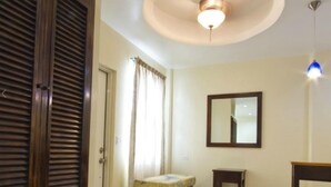 A room with a ceiling fan, a mirror, a small table, and a window with curtains. - Rainbow Hotel (Caye Caulker)