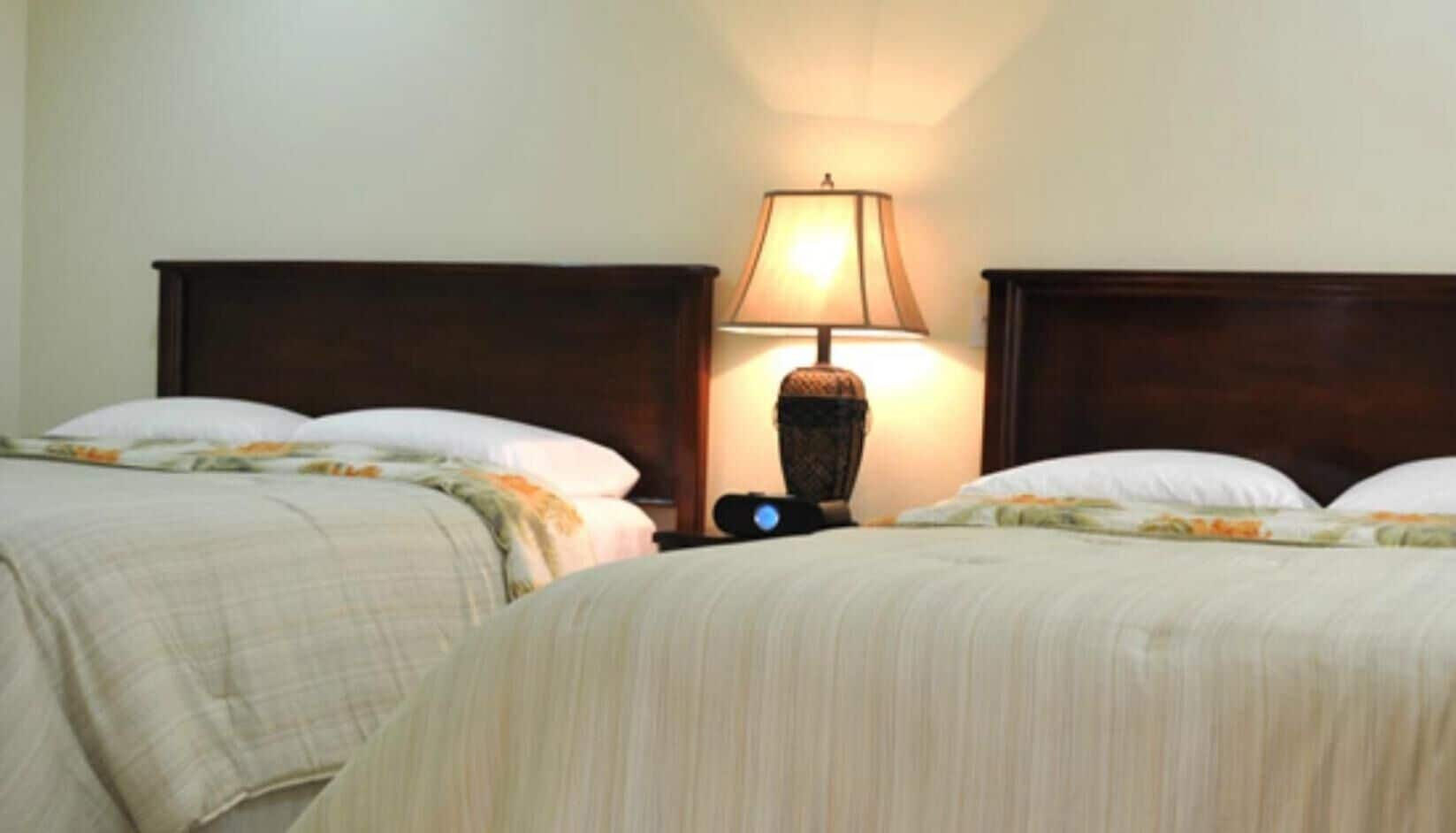 Une chambre d’hôtel avec deux lits, une table de chevet avec une lampe et une horloge fixée au mur.