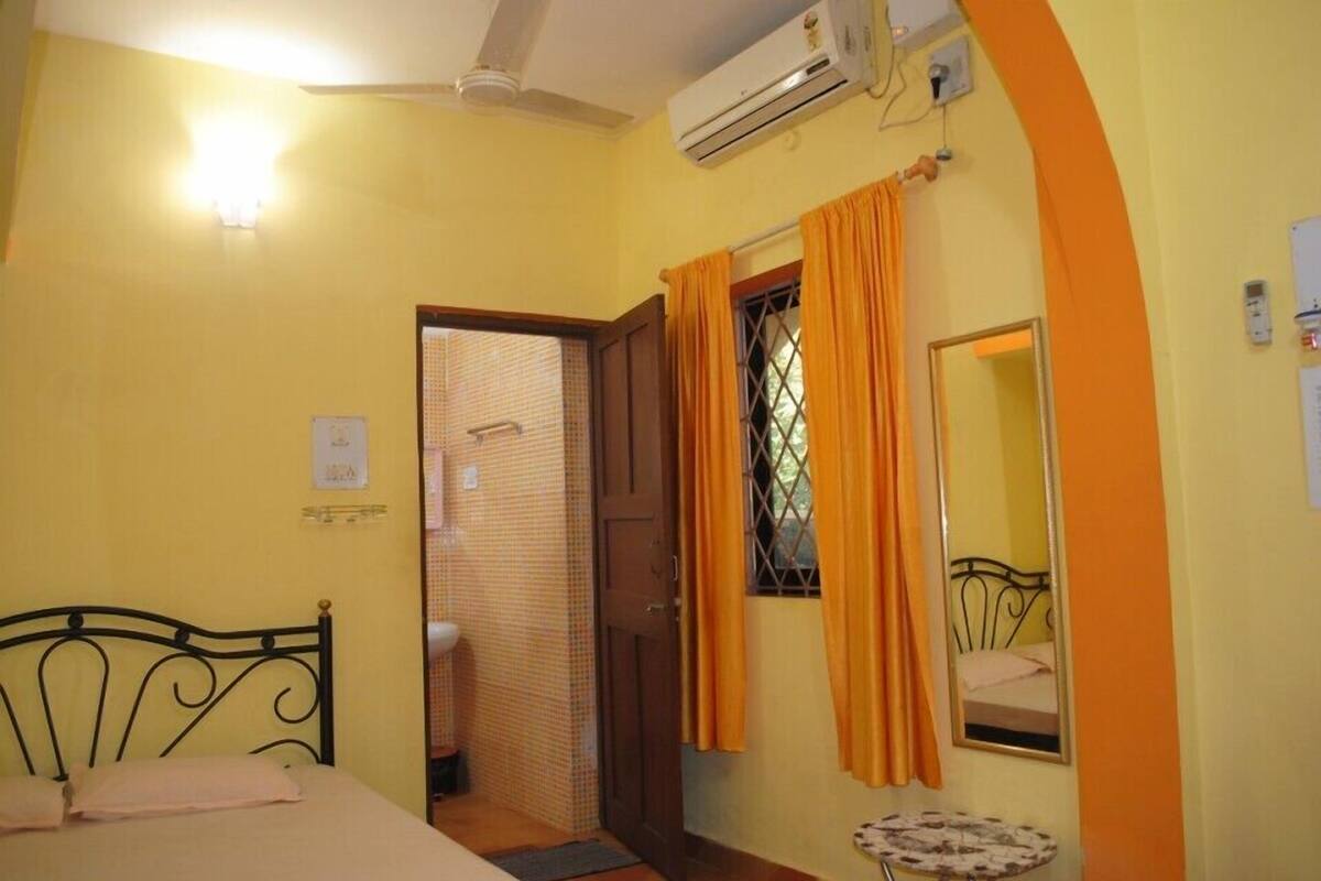A room with a bed, an air conditioning unit, a small table, and a window with curtains.