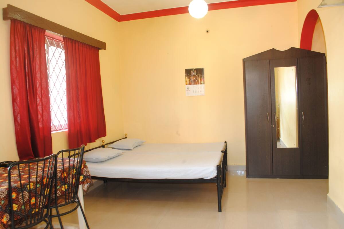 A room with a bed, a table with chairs, a wardrobe, and a calendar on the wall.
