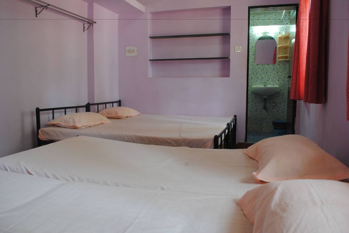 A room with two single beds, a small shelf unit, and a bathroom visible through an open door.